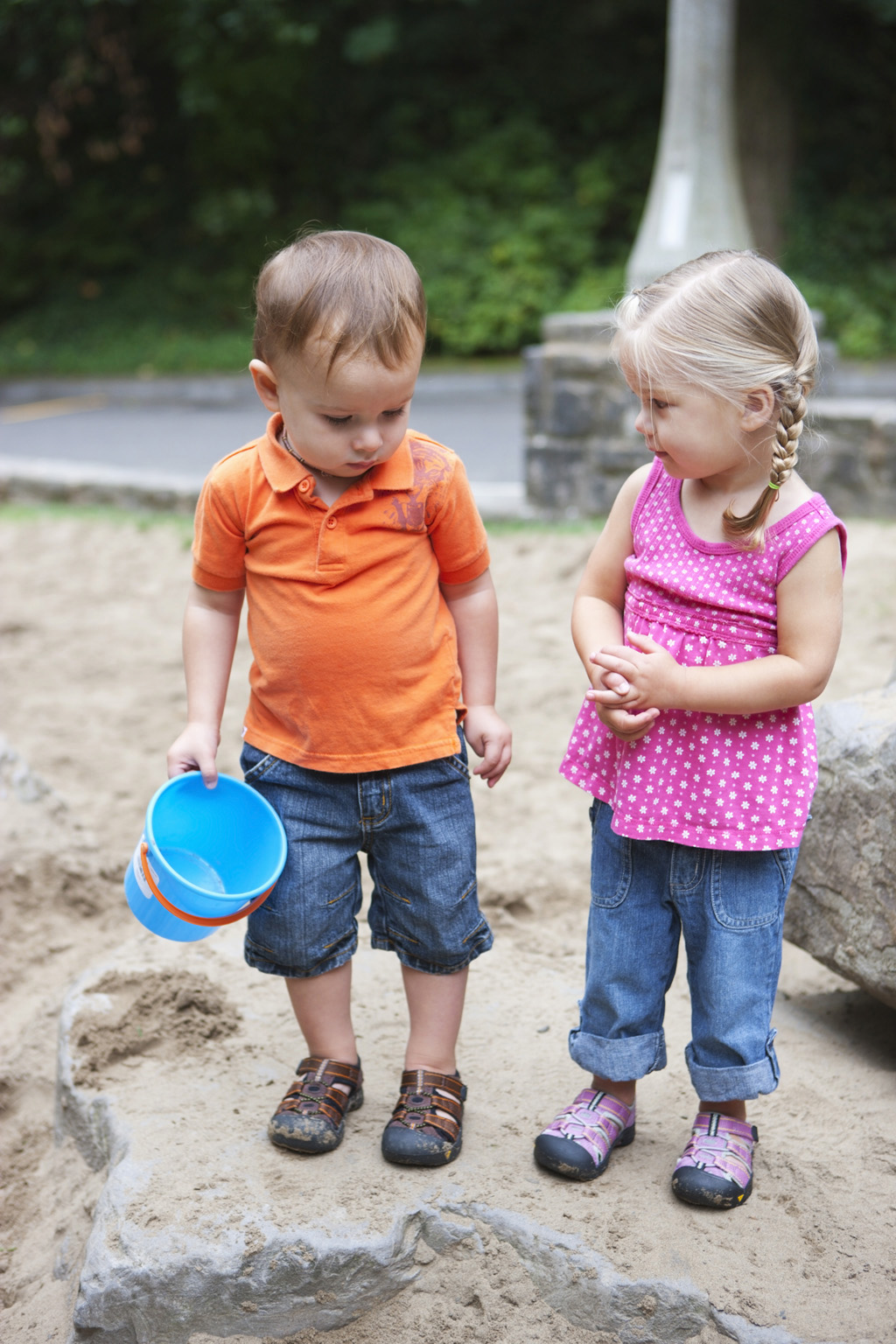 Small boy and girl in standing in sand box.