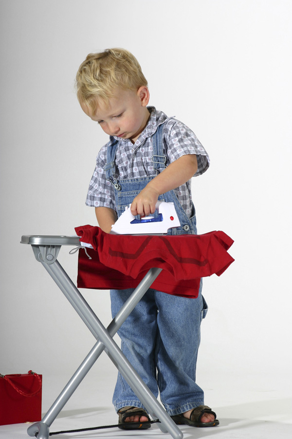 A young boy plays with a pretend iron and ironing board.