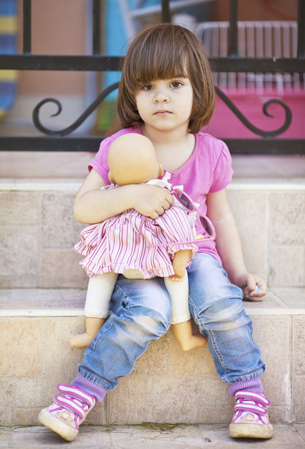 Little girl sitting on step with baby doll, looking sad.