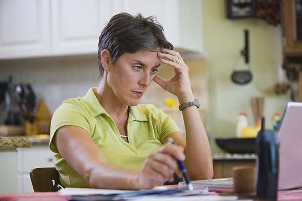 Woman sits with laptop and papers at kitchen table.